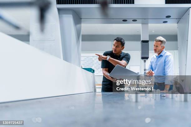 engineer with laptop pointing by businessman at factory - engineer factory stock pictures, royalty-free photos & images