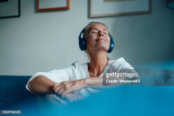 smiling woman listening music through headphones at home - hören stock-fotos und bilder