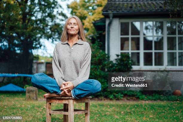 woman practicing yoga on stool at backyard - yoga stock-fotos und bilder