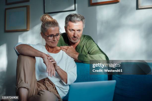 couple watching laptop on sofa at home - couple 50 55 laptop stock-fotos und bilder