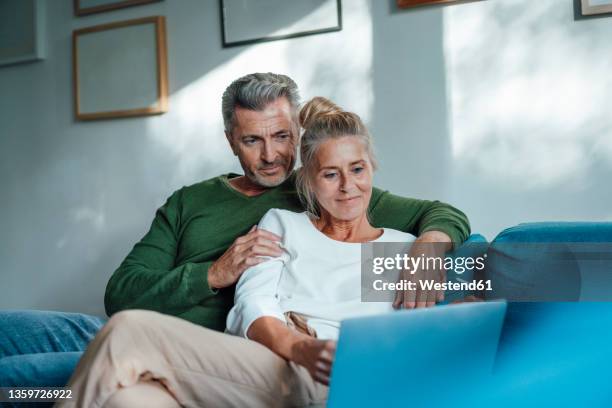 couple using laptop sitting on sofa together at home - couple 50 55 laptop stock-fotos und bilder