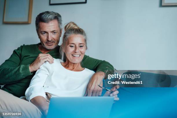 happy couple using laptop on sofa - couple 50 55 laptop stock-fotos und bilder