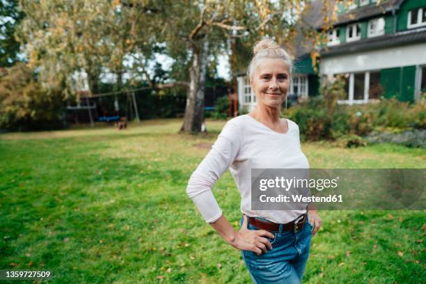 smiling woman with hands on hip standing at backyard - handen op de heupen stockfoto's en -beelden