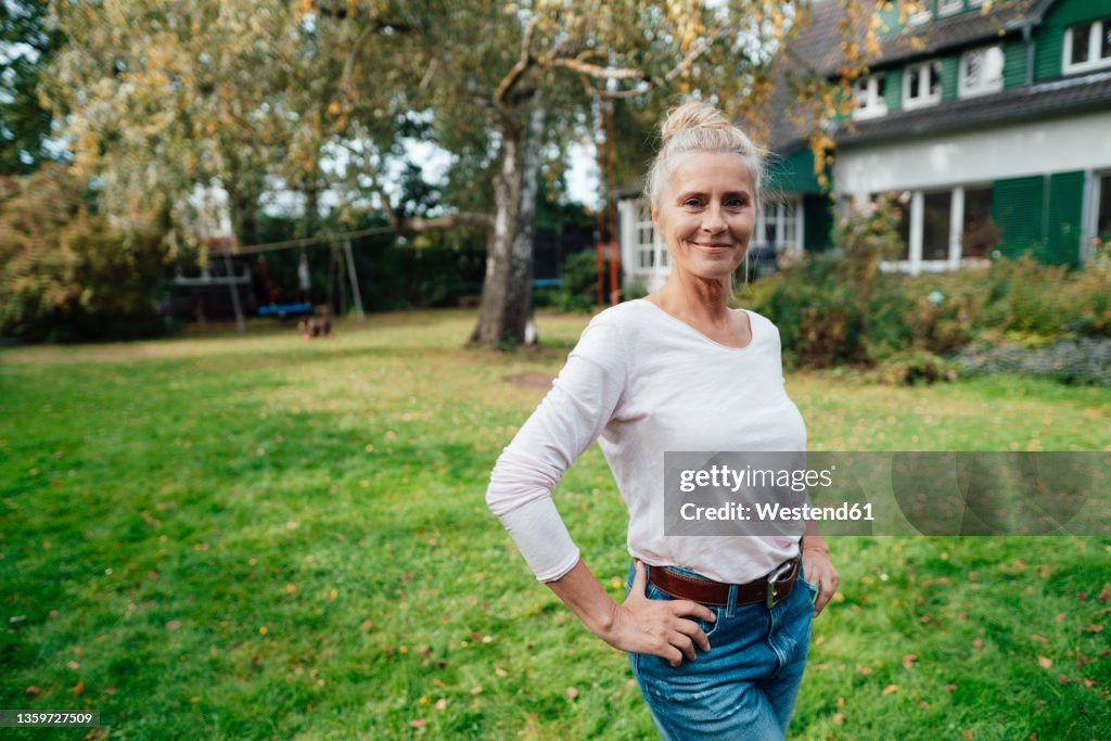 Smiling woman with hands on hip standing at backyard