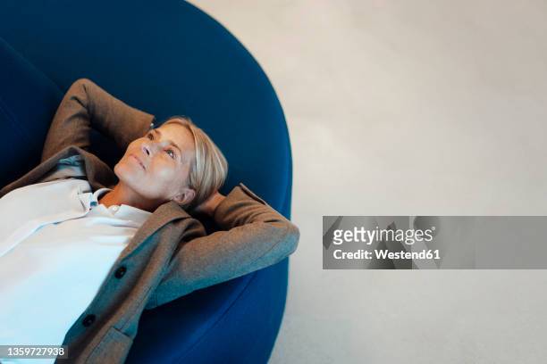 businesswoman with hands behind head resting in office - businesswoman couch fotografías e imágenes de stock