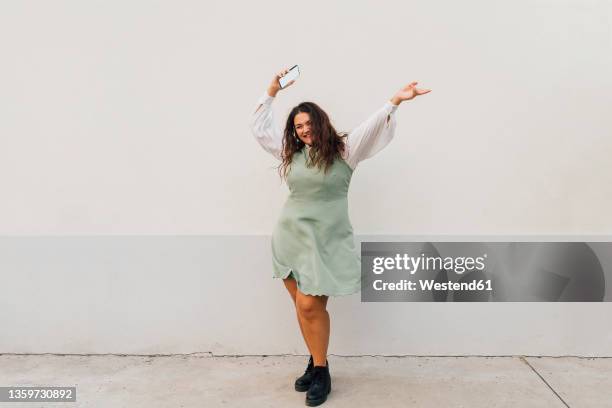cheerful plus size woman with smart phone dancing against wall - fat woman dancing stock pictures, royalty-free photos & images