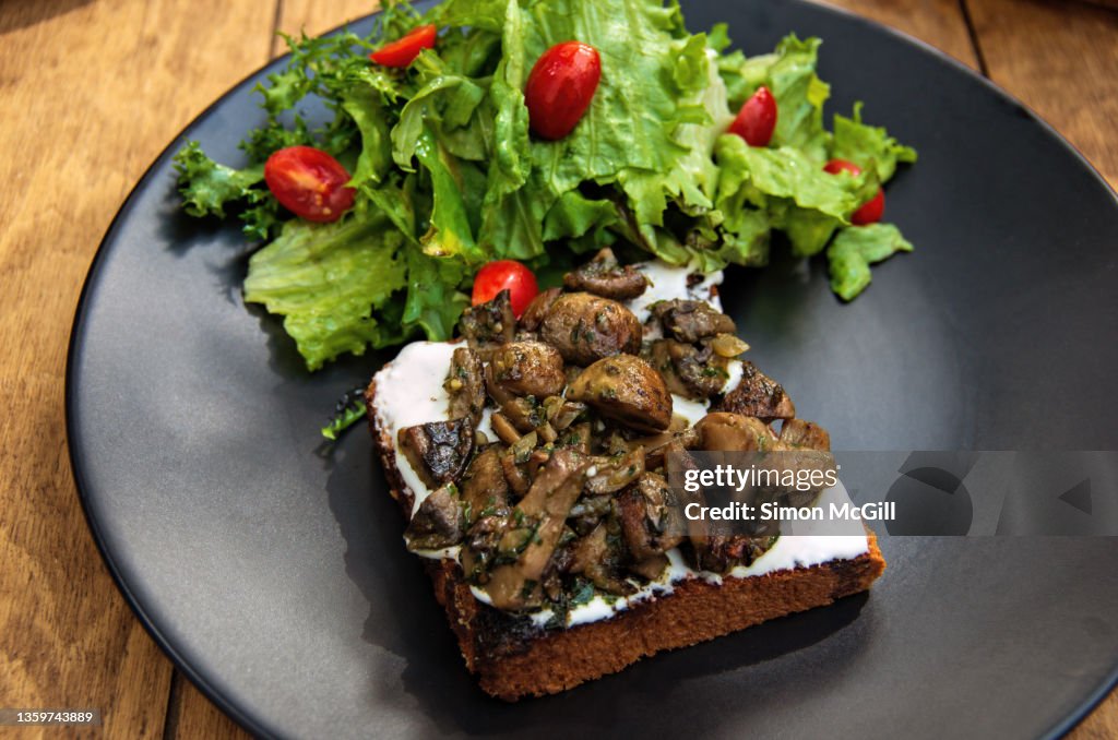 Toasted bread with a cream spread, roasted mushrooms with pesto and fried onions, and a side salad of red grape tomatoes and lettuce