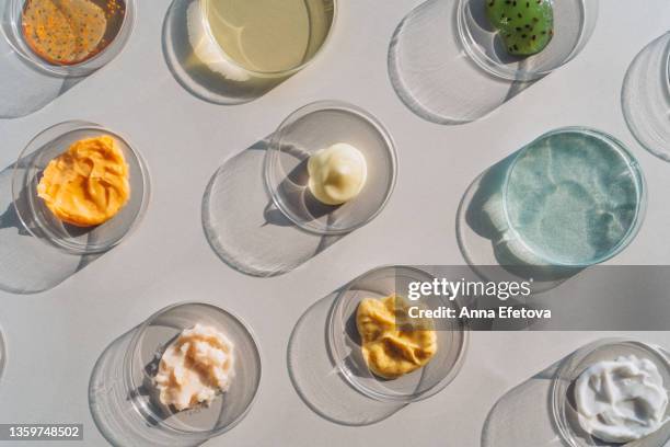 background made with different beauty products in many petri dishes. face serums, gel, scrubs and a lot of multicolored creams. concept of cosmetics laboratory researches. photography in flat lay style - petri dish stock-fotos und bilder