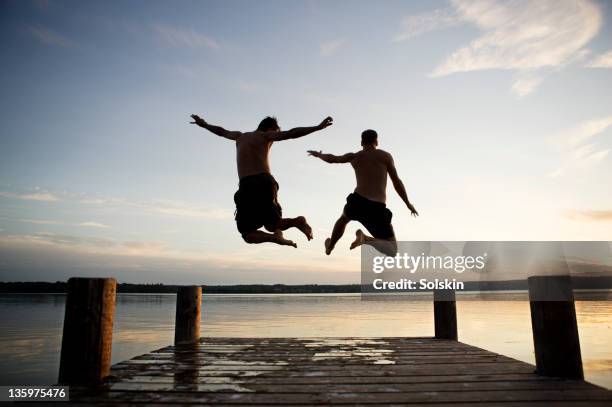 two men jumping into lake from jetty - summer denmark stock pictures, royalty-free photos & images