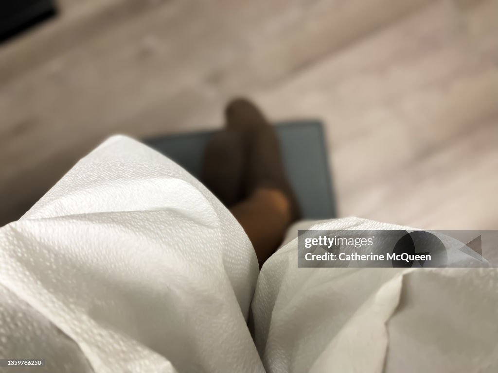 African-american woman wearing patient gown stares down at feet while waiting for doctor in examination room