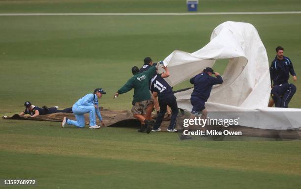 Players and grounds crew work together to cover the wicket with rain covers as rain delays play during the WNCL match between Victoria and New South...
