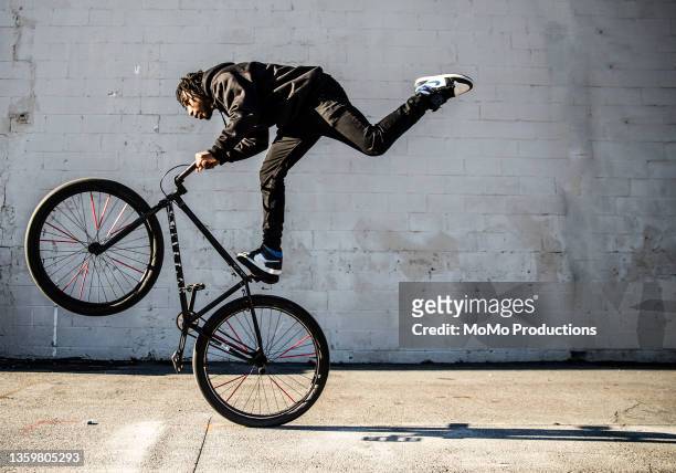 young male bmx rider performing wheelie in urban area - modern boy hipster stock pictures, royalty-free photos & images