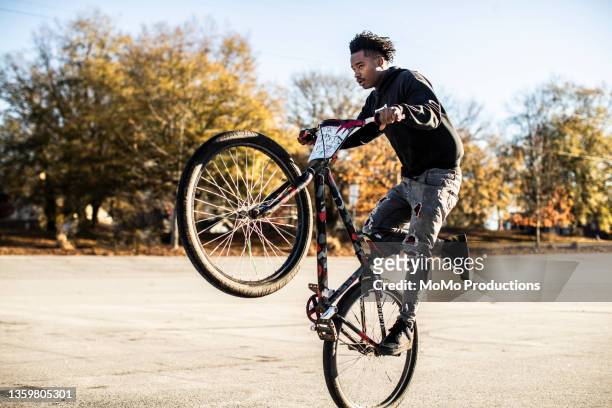 young male bmx rider performing wheelie in urban area - wheelie stock-fotos und bilder
