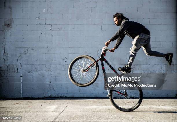 young male bmx rider performing wheelie in urban area - ciclismo bmx imagens e fotografias de stock