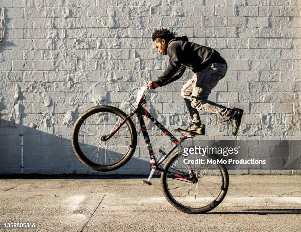 young male bmx rider performing wheelie in urban area - wheelie stockfoto's en -beelden