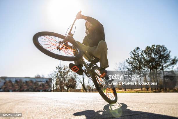 young male bmx rider performing wheelie in urban area - stunt stock pictures, royalty-free photos & images