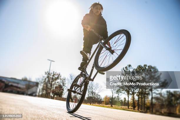 young male bmx rider performing wheelie in urban area - bmx stock-fotos und bilder