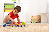 Cute little boy playing with colorful toys on floor at home, space for text