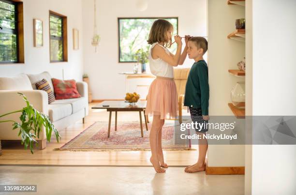 ragazza che misura l'altezza di suo fratello minore contro un muro a casa - alto foto e immagini stock