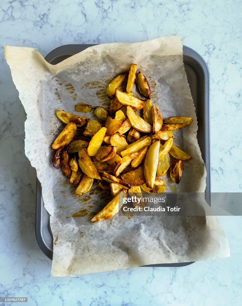 Tray of roasted potatoes on parchment paper on white, marble background