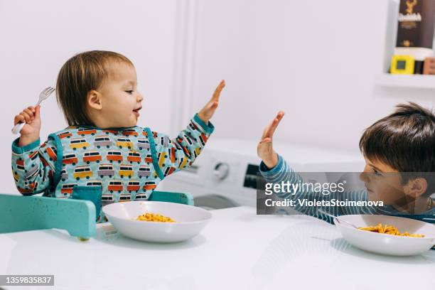 cute children eating spaghetti for dinner and making a mess. - sisters feeding bildbanksfoton och bilder