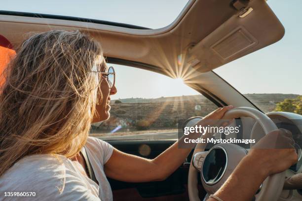 young woman driving car at sunset, road trip concept - car rental stockfoto's en -beelden