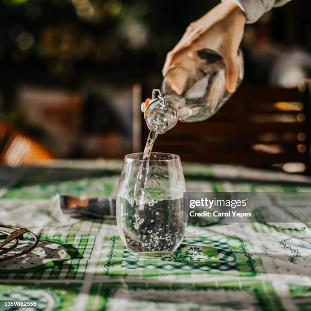 a hand pouring fresh water  from a bottle into a cut glass tumbler - glass of water hand ストックフォトと画像