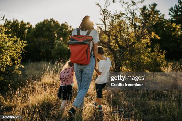 rückansicht der mutter, während sie händchen hält und mit ihren beiden kindern in der natur spazieren geht - girls hands behind back stock-fotos und bilder