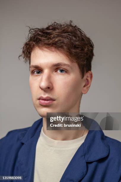 retrato de estudio de cerca de un hombre de 23 años con cabello castaño en camisa azul sobre fondo gris - cabello-castaño fotografías e imágenes de stock