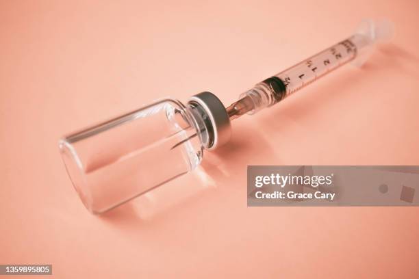syringe with needle inserted into medical vial on orange background - liquid solution stock pictures, royalty-free photos & images