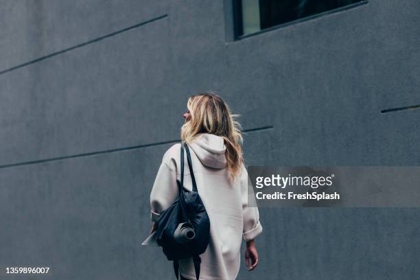una mujer irreconocible caminando por la calle, yendo a su entrenamiento - hooded shirt fotografías e imágenes de stock