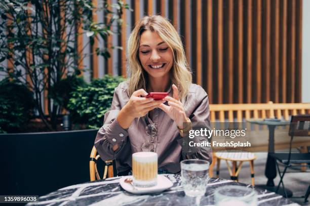 eine glückliche frau, die ein foto von ihrem getränk macht, während sie in einem café sitzt - effortless stock-fotos und bilder