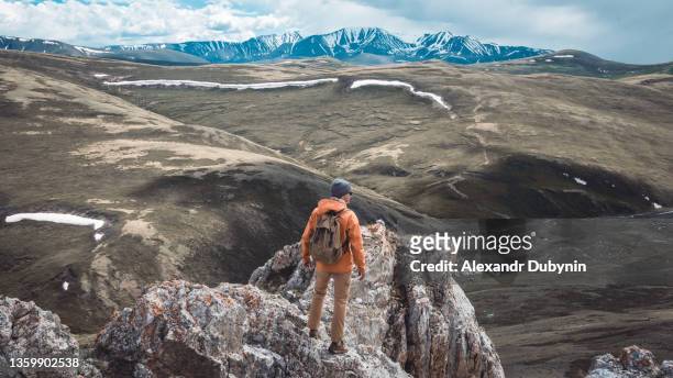 a man a tourist with a backpack on top of a mountain with a panoramic view of the mountains. travel concept - higher return stock pictures, royalty-free photos & images