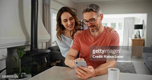 shot of a couple looking at something on a cellphone together at home - couple smartphone stock pictures, royalty-free photos & images