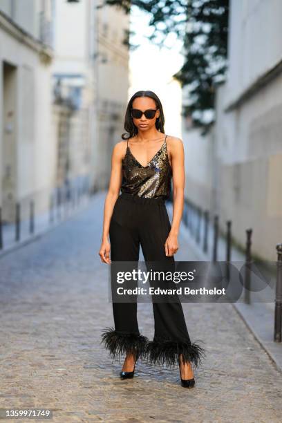 Emilie Joseph @in_fashionwetrust wears black sunglasses, a black sequined / shiny glitter V-neck tank-top, silver earrings, high waist black large...