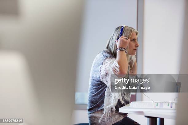 mature female student adjusting headphones at computer - computer training stock pictures, royalty-free photos & images