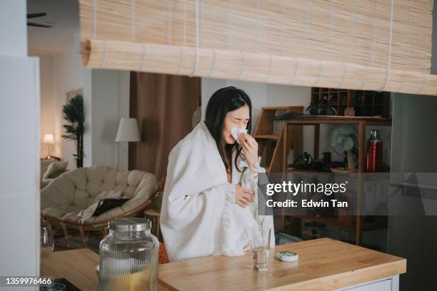 asian chinese woman covered with blanket having  cold and flu taking medicine from daily pill organizer at kithen counter home - allergy medicine stock pictures, royalty-free photos & images