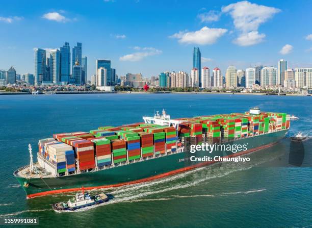 drone point view of large cargo ship in front of qingdao city skyline, shandong province, china - qingdao stock-fotos und bilder