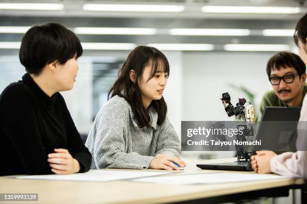 employees of a start-up company examining a robot prototype - 20s talking serious bildbanksfoton och bilder