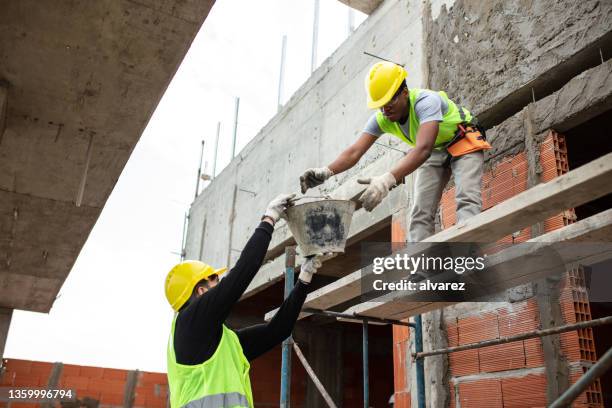 two workers working together at new construction site - reaching higher stock pictures, royalty-free photos & images
