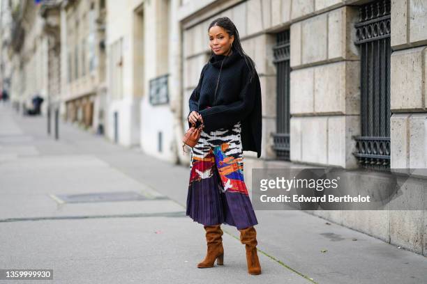 Ellie Delphine wears a black braided ribbed wool turtleneck oversized pullover, a high waits white with black and gold print pattern and purple blue...