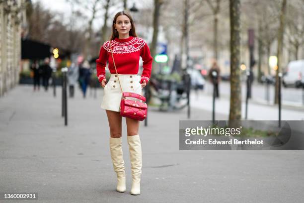 Diane Batoukina wears a red with white embroidered Christmas pattern wool pullover, white wool / tweed pleated shorts, rings, a red shiny quilted...