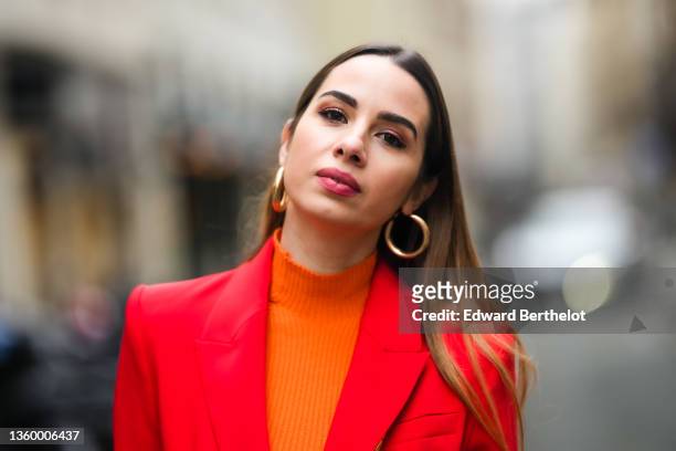 Maria Rosaria Rizzo wears gold large earrings, a neon orange ribbed turtleneck pullover, a neon red blazer jacket, during a street style fashion...