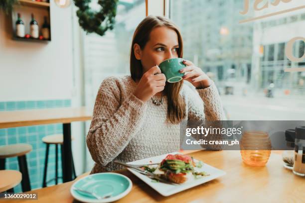 woman drinking coffee and eating avocado toast in the restaurant - brunch restaurant stockfoto's en -beelden