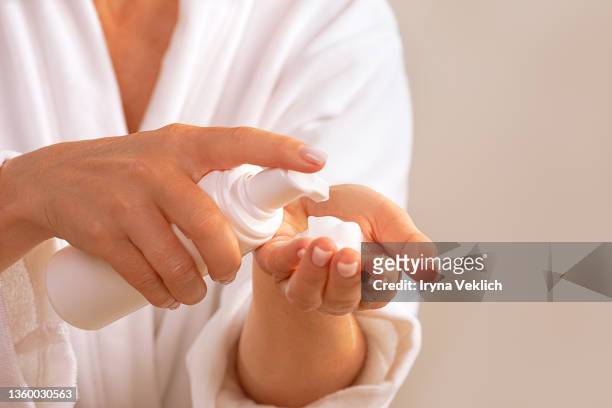beautiful woman in white bathrobe holds beauty product soap or cosmetic milk or washing foam. - foam hand imagens e fotografias de stock