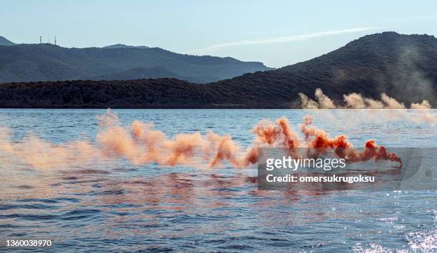 one orange colored smoke grenade in the blue sea. distress call - distress flare stock pictures, royalty-free photos & images