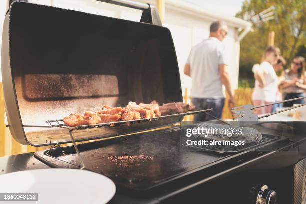 close-up of side view of pig grilling on hot griddle in the backyard against a group of unrecognizable people in the background during a sunny afternoon - gusseiserne pfanne stock-fotos und bilder