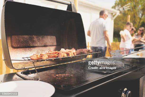 close-up of side view of pig grilling on hot griddle in the backyard against a group of unrecognizable people in the background during a sunny afternoon - griddle stock pictures, royalty-free photos & images
