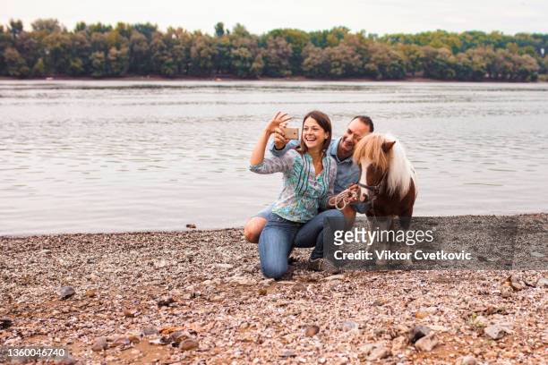jeune couple avec poney prenant un selfie au bord du lac - agriculteur selfie photos et images de collection