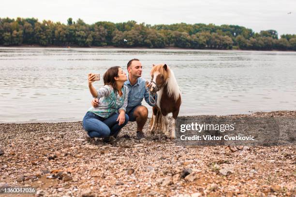 jeune couple avec poney prenant un selfie au bord du lac - agriculteur selfie photos et images de collection